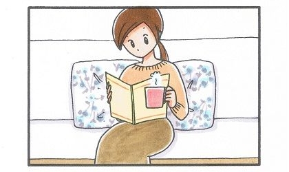 ソファに座ってコーヒーを飲みながら本を読む飼い主